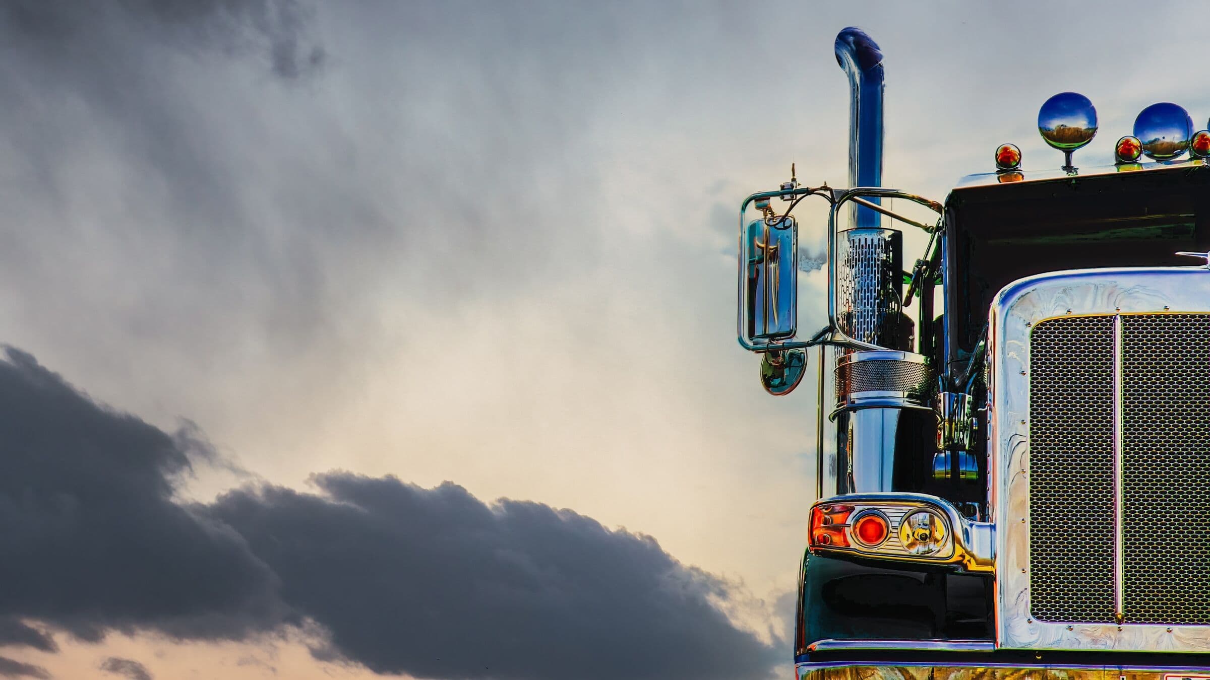 The chrome grille and lights of a black semi truck under a stormy sky